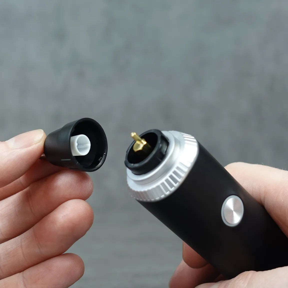 Close-up of a hand holding a nose and ear hair trimmer body and detachable head against a grey background.