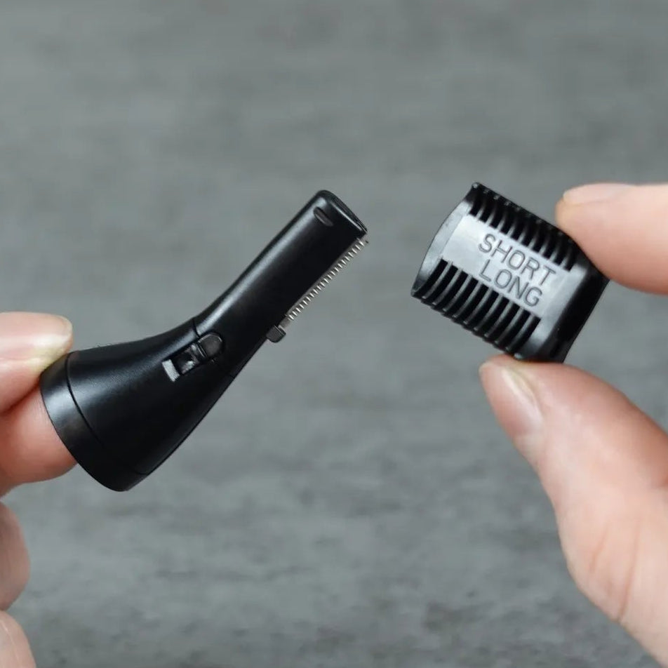Two hands holding a black eyebrow trimmer head and comb on a gray background