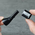 Two hands holding a black eyebrow trimmer head and comb on a gray background
