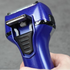 Blue electric shaver held in a hand against a gray background, showing pop-up trimmer