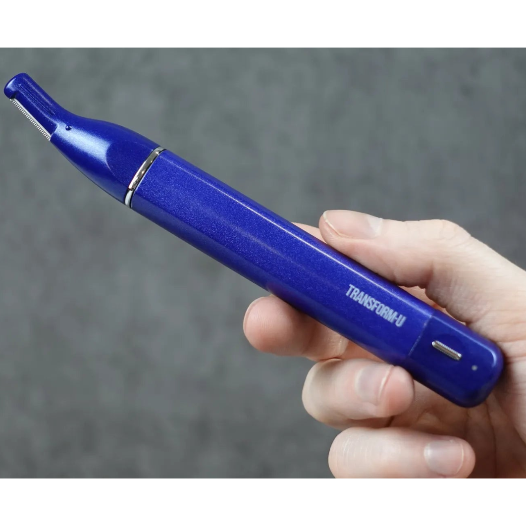 Hand holding a blue nose and ear trimmer hair device labeled 'TRANSFORM-U' against a gray background