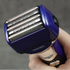Hand holding a blue electric shaver with visible brand name against a gray background