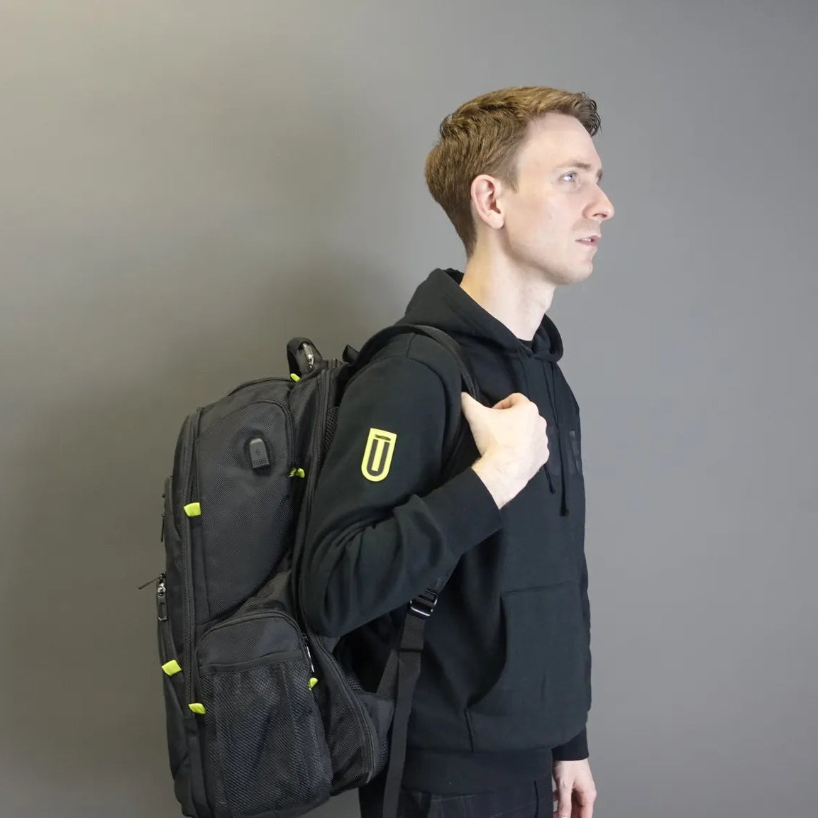 Person wearing a black backpack with a logo on a gray background