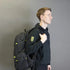 Person wearing a black backpack with a logo on a gray background