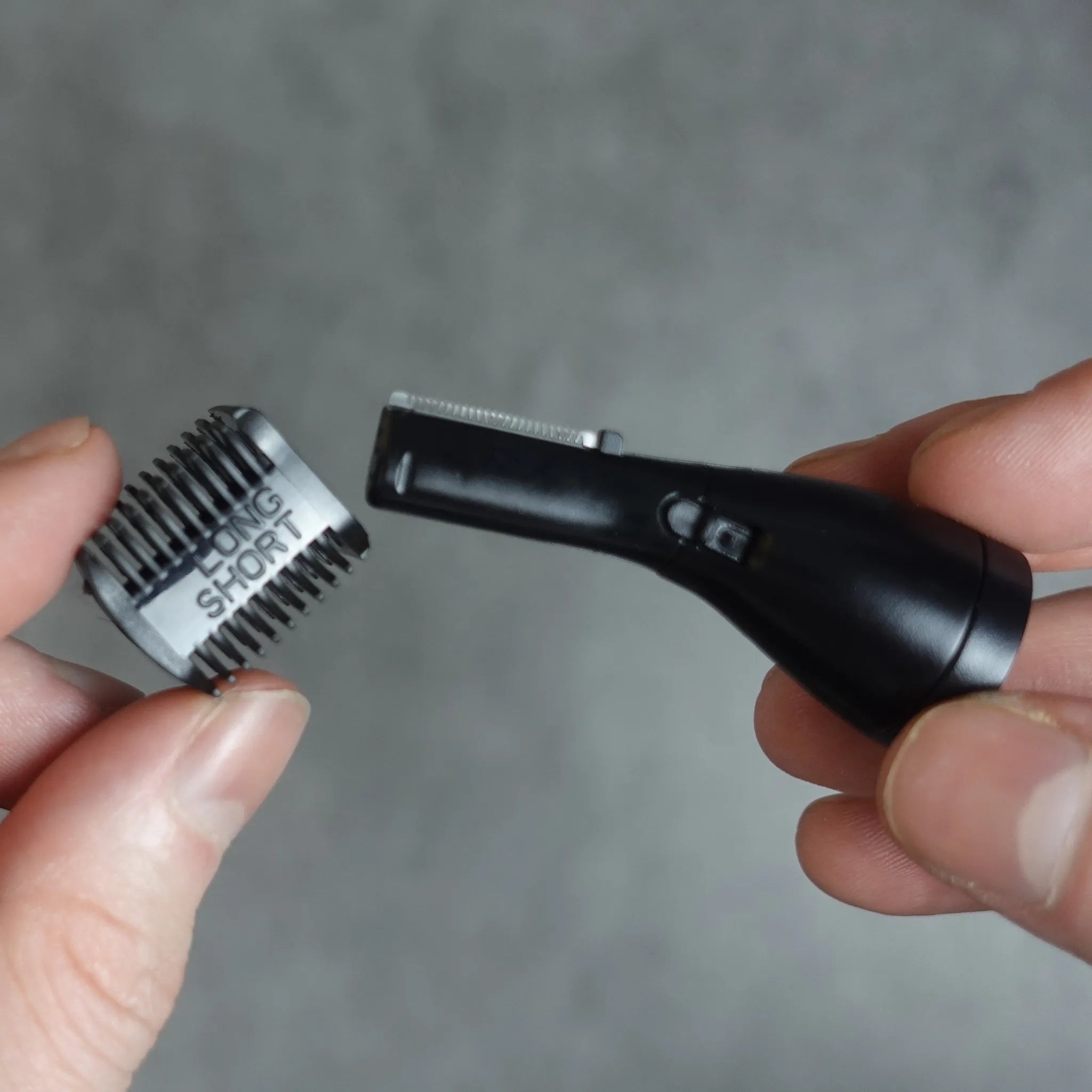 Nose and ear hair trimmer with an eyebrow comb attachment held by a hand against a gray background