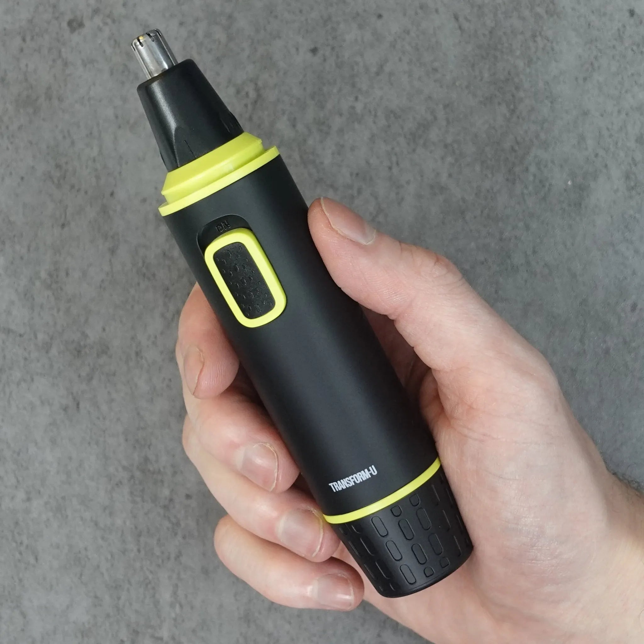 Hand holding a black and green nose and ear hair trimmer against a gray background
