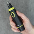 Hand holding a black and green nose and ear hair trimmer against a gray background