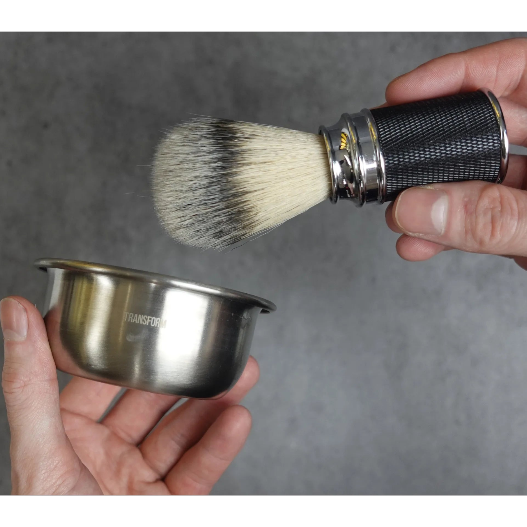 Shaving brush and bowl held by hands against a gray background
