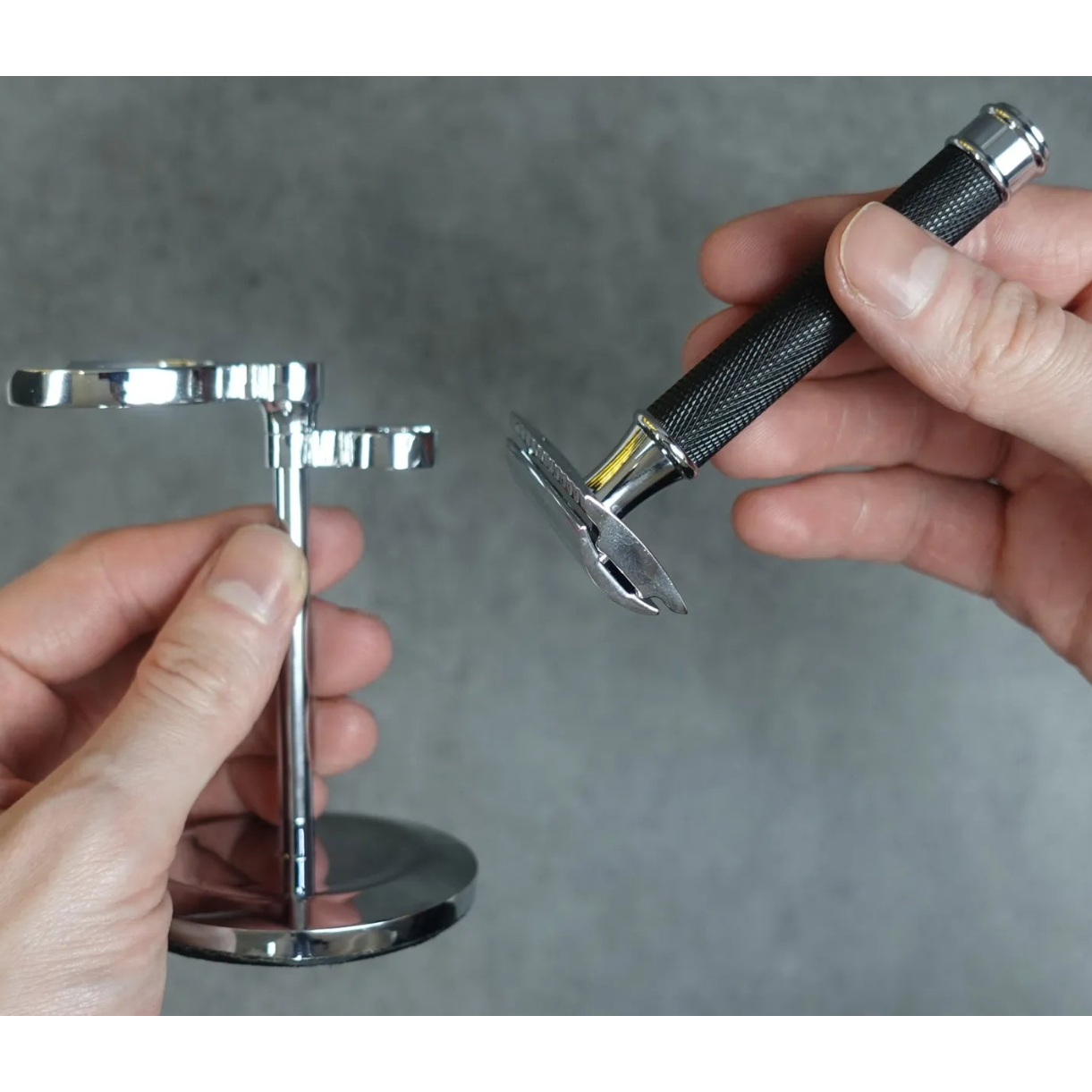 Person holding a metal safety razor stand against a gray background