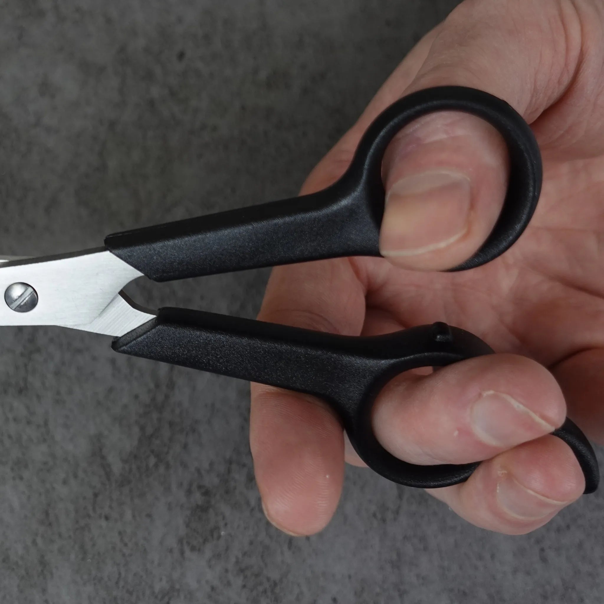 Hand holding a pair of black-handled scissors against a gray background