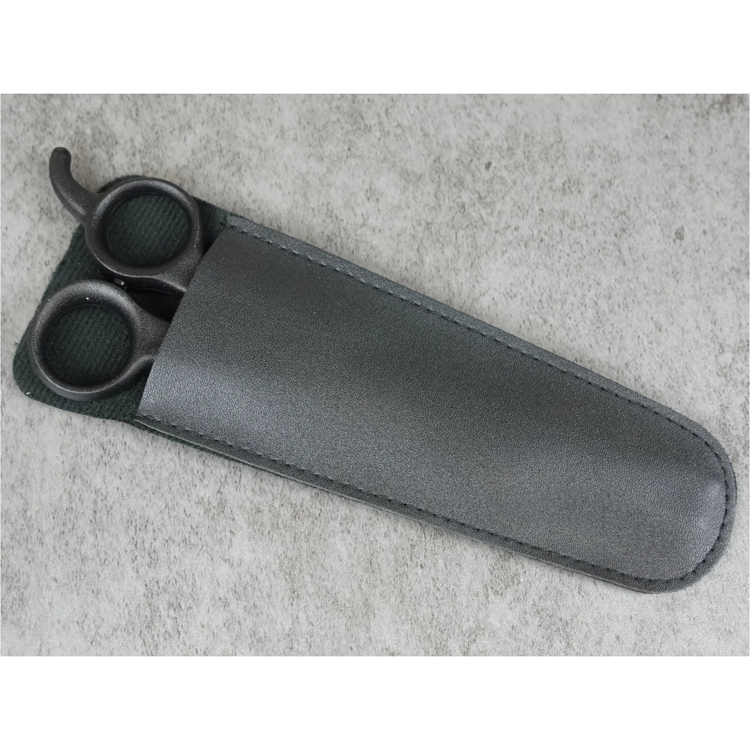 Black scissors in a matching sheath on a gray concrete surface