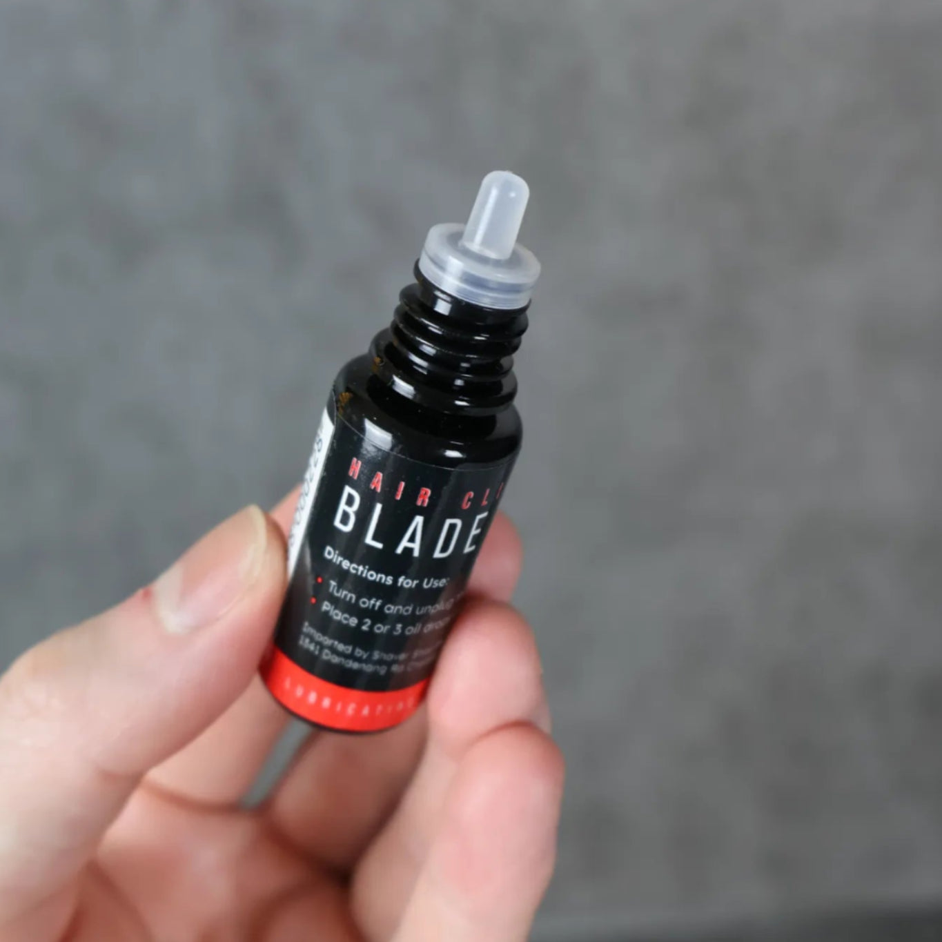 Hand holding a small black blade oil bottle against a gray background