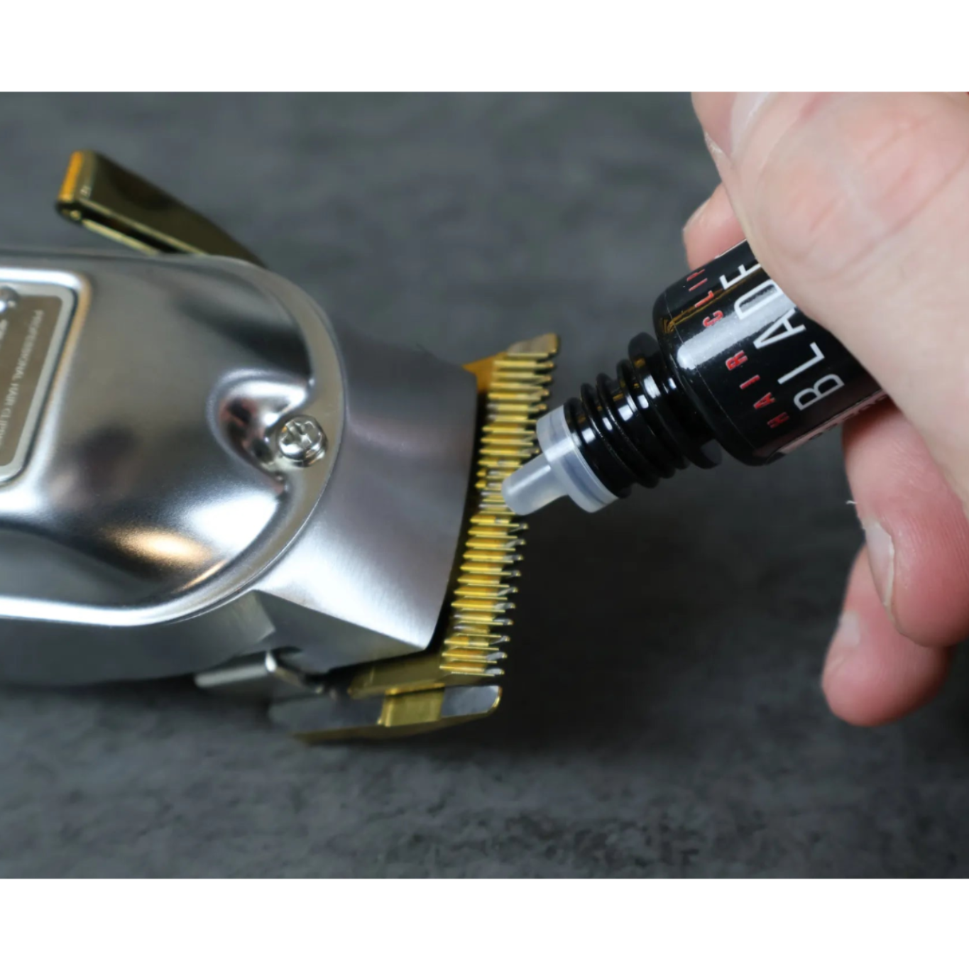 Person using blade oil on a hair clipper against a gray background