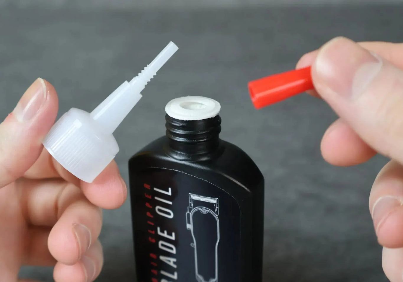 Person holding red cap and clear nozzle for blade oil bottle on a dark background