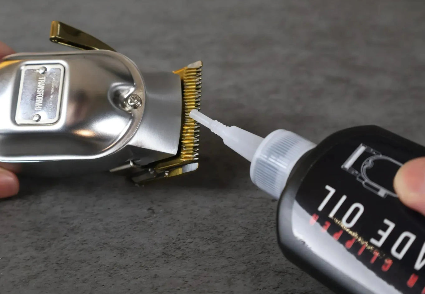 Hair clipper with a bottle of oil being applied on a dark surface