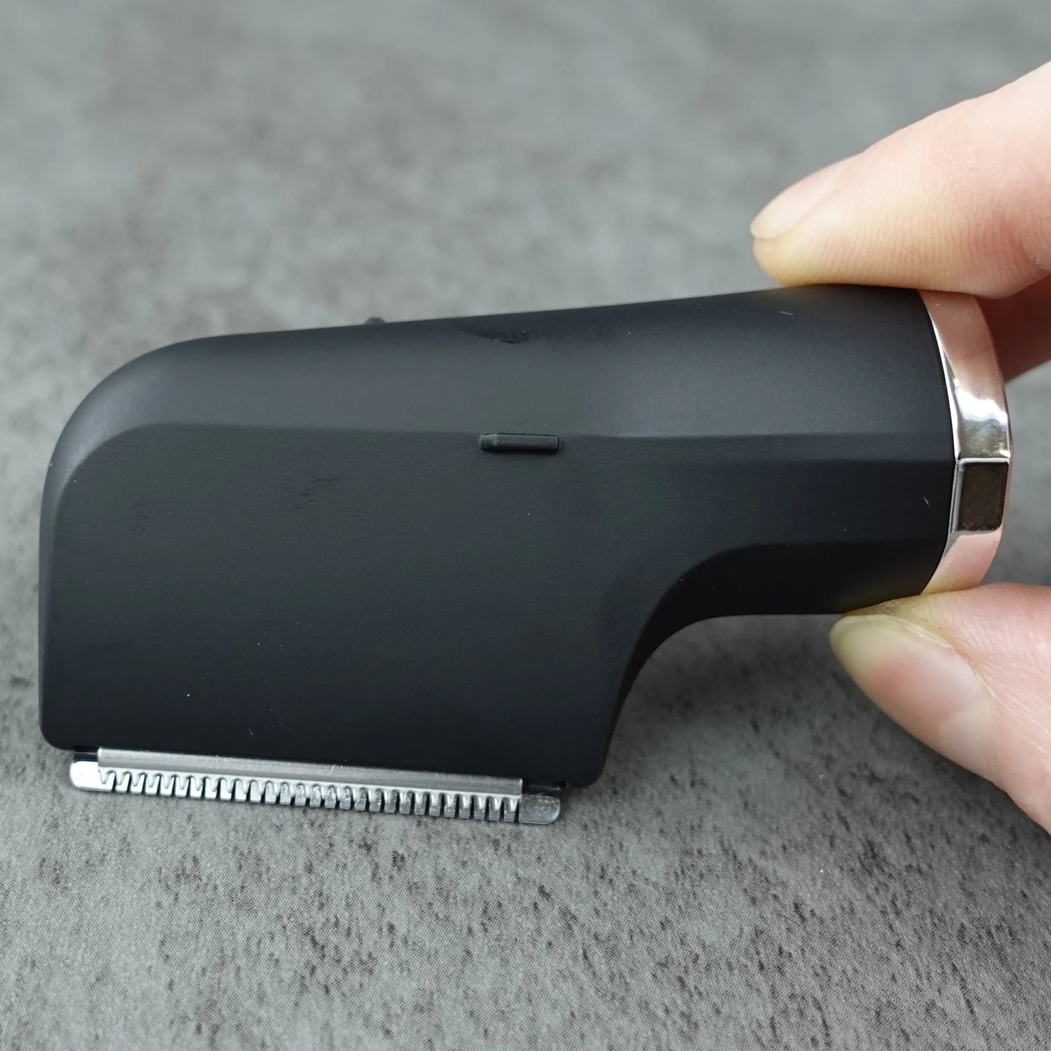 Small black grooming tool held by a hand on a gray surface