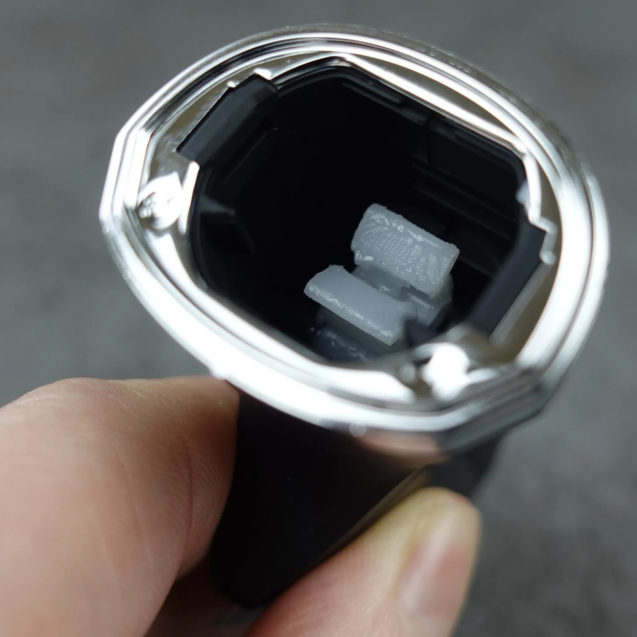 Close-up of a hand holding a black body groomer showing interior on a gray background