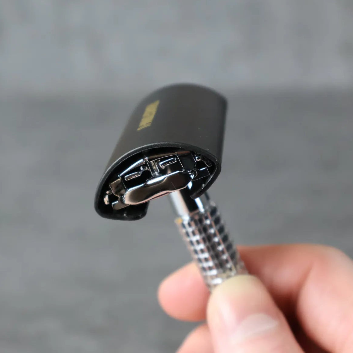 Hand holding a safety razor with protective cover on against a gray background