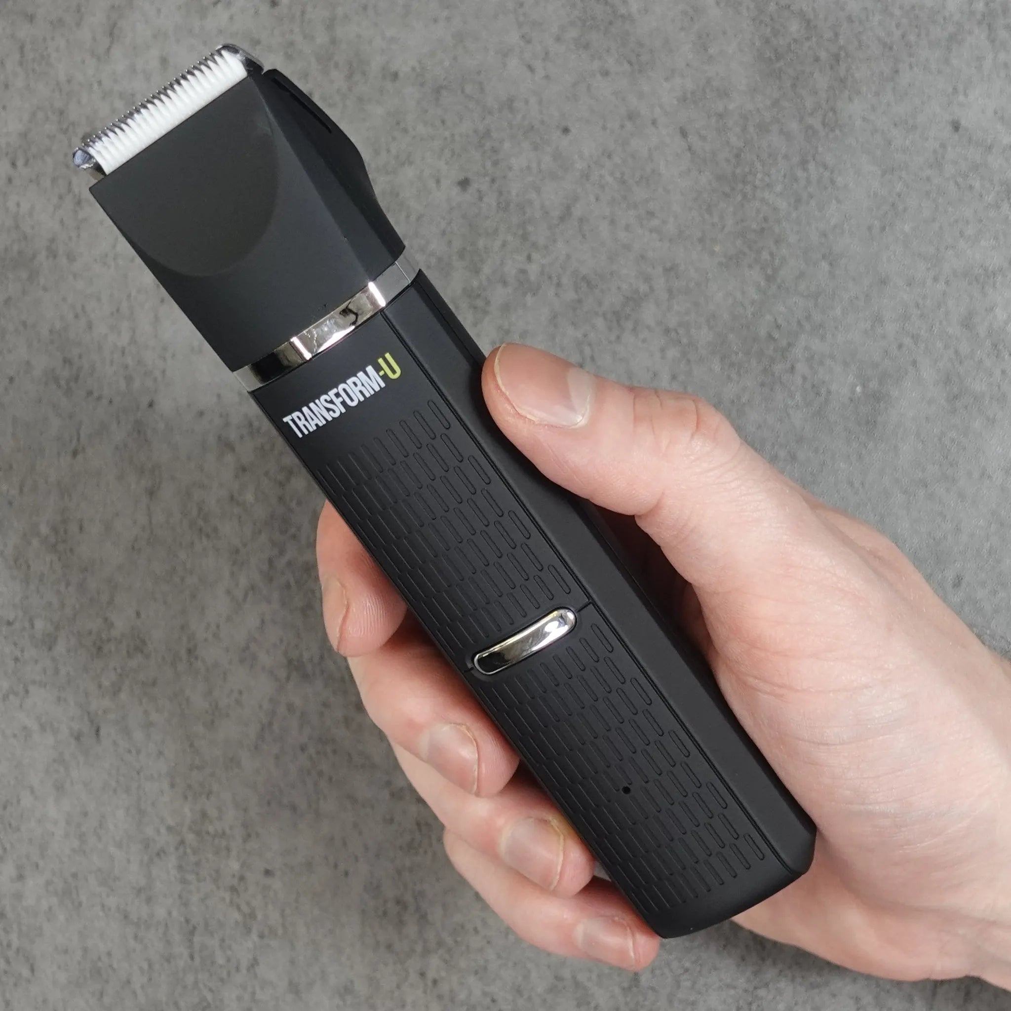 Hand holding a black body grooming tool with 'Transform-U' branding on a gray background