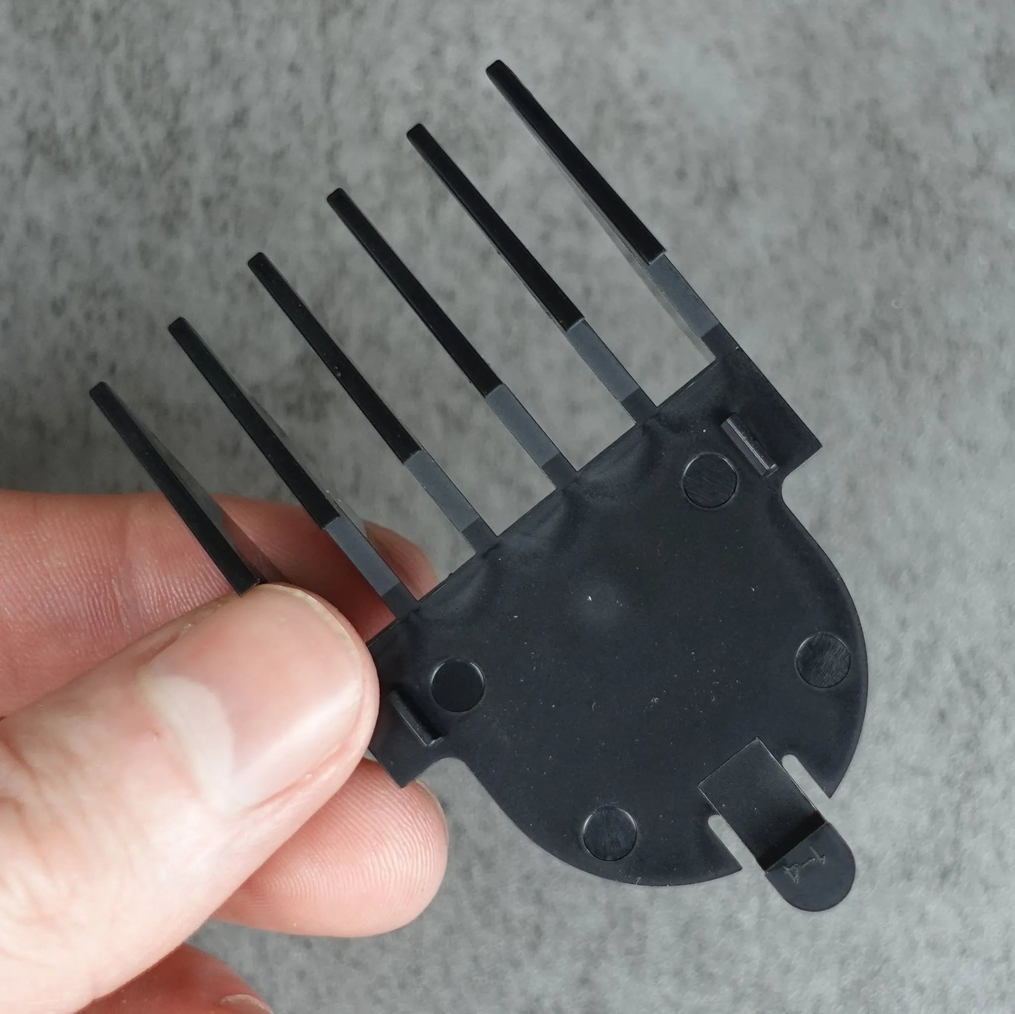 Black beard trimmer comb held by a hand against a gray background