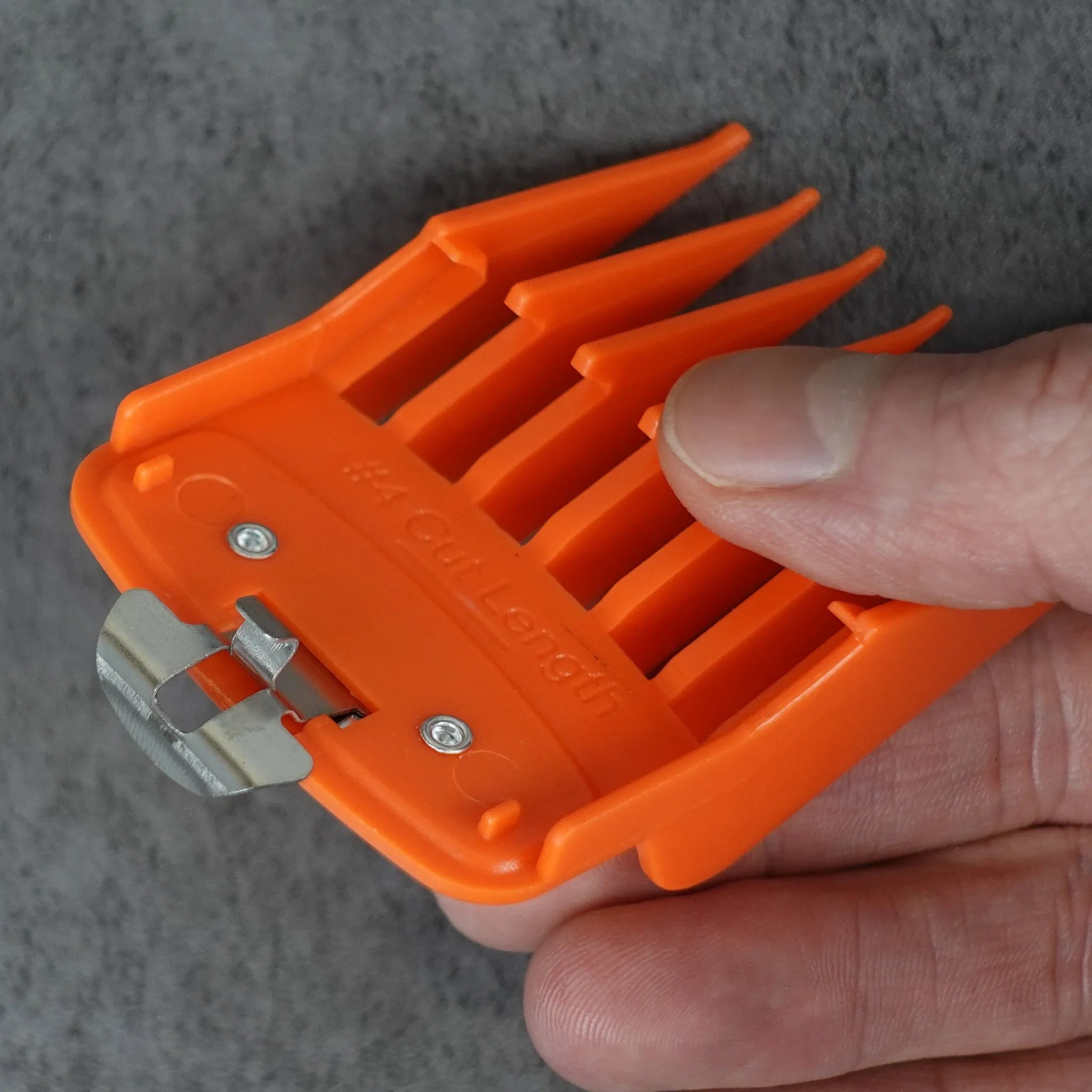 Orange hair clipper guide comb held by a hand on a gray background