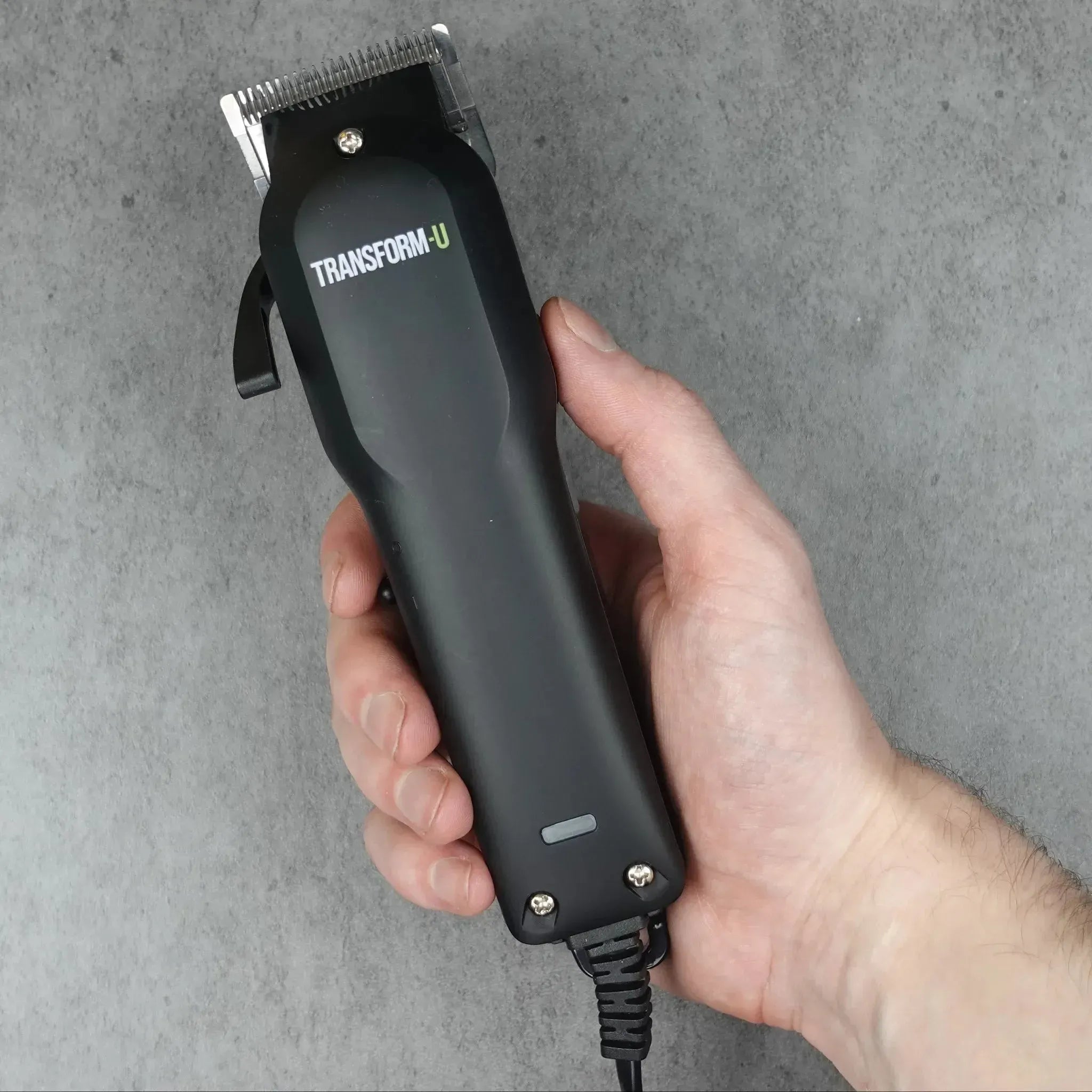 Hand holding a black hair clipper with 'Transform U' branding on a gray background