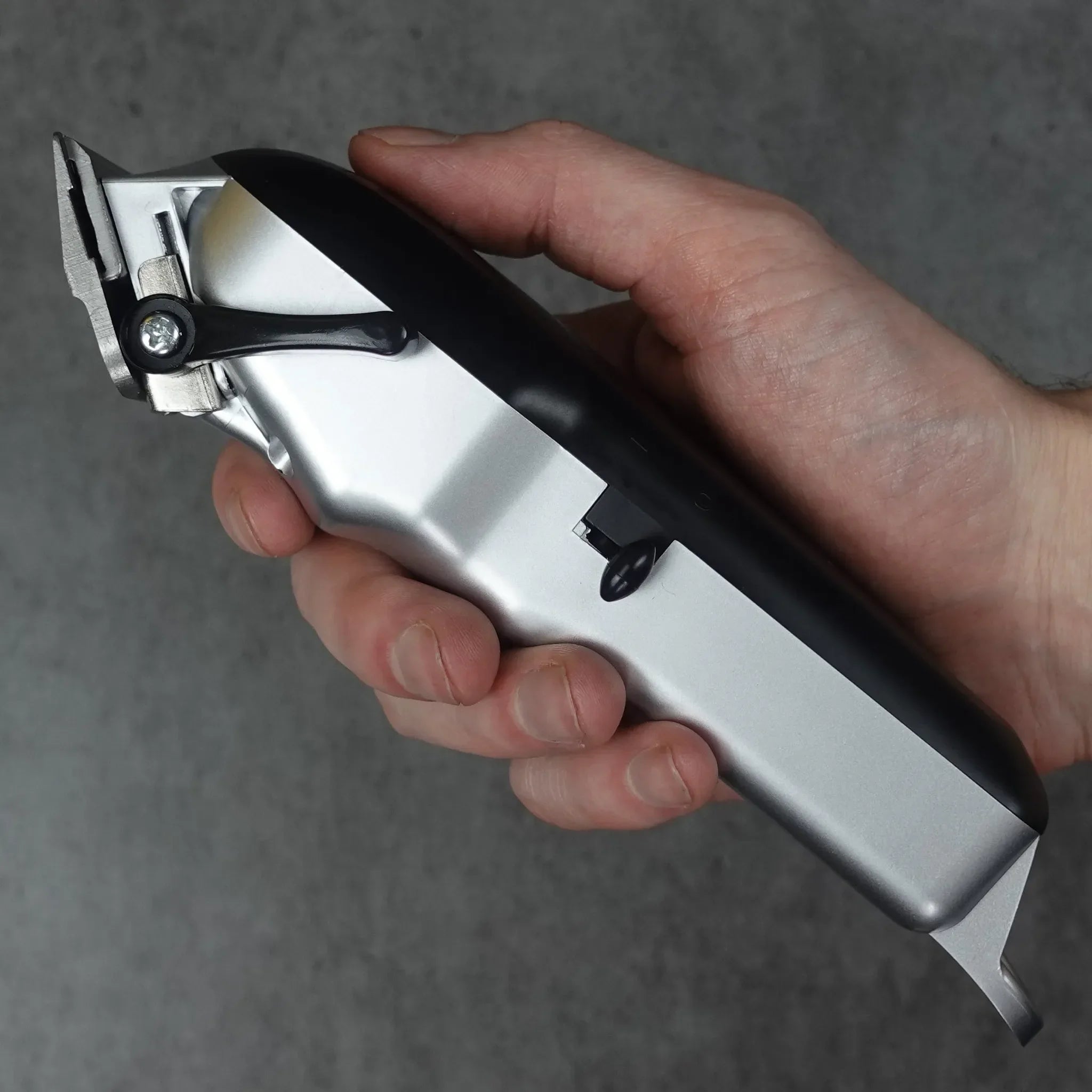 Hand holding a silver and black hair clipper against a gray background