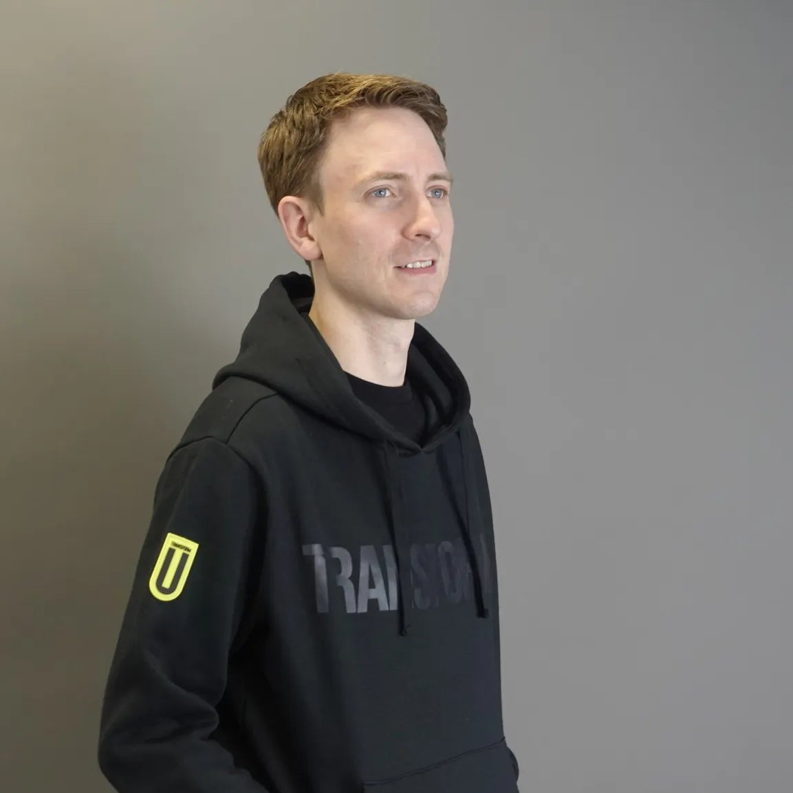 Man wearing a black hoodie with a logo on a gray background