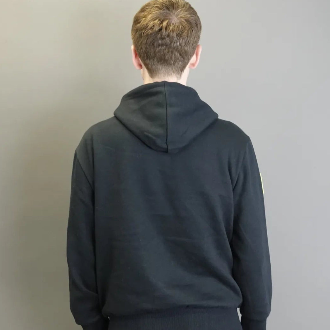 Person wearing a black hoodie from behind against a plain background