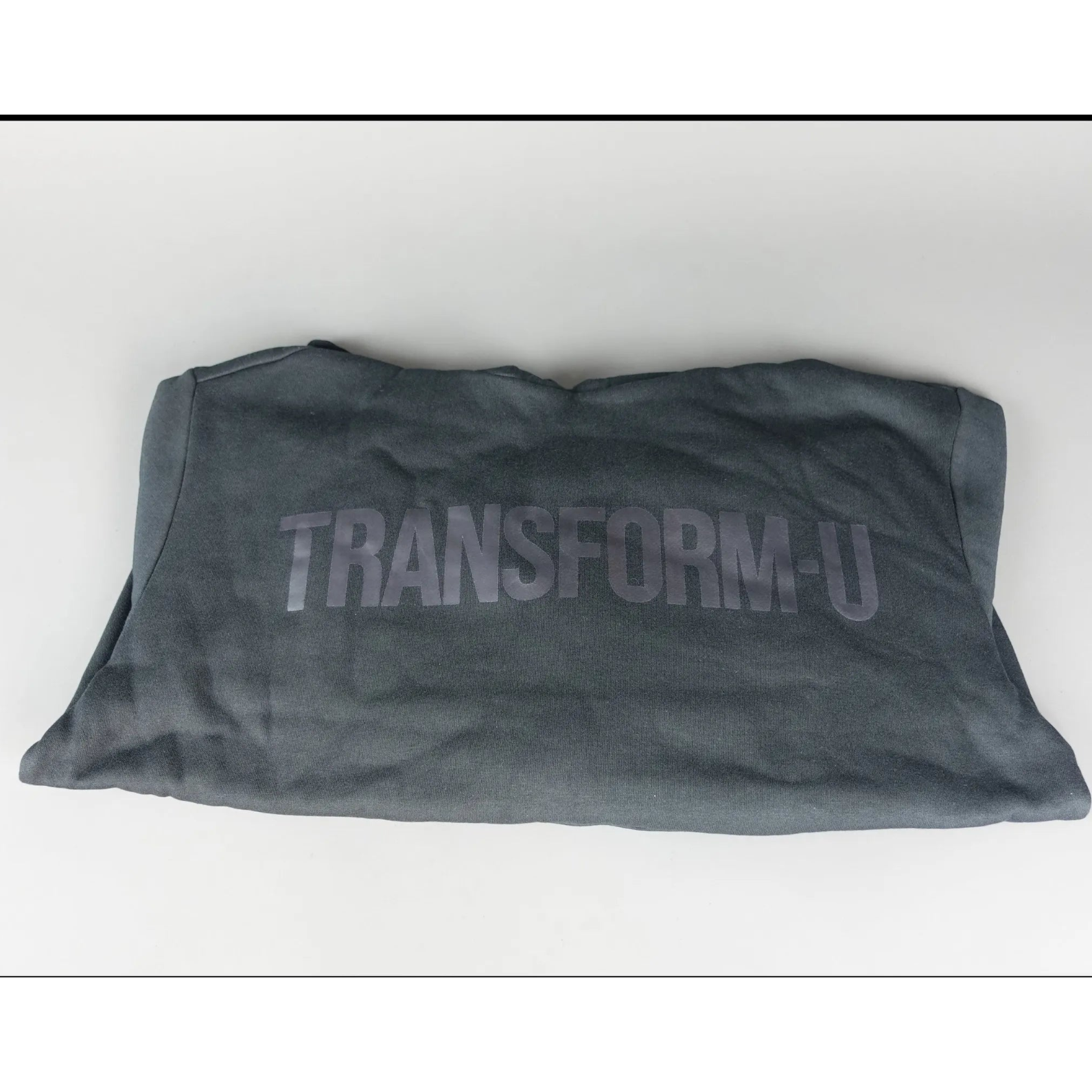 Folded gray hoodie with 'TRANSFORM-U' text on a white background