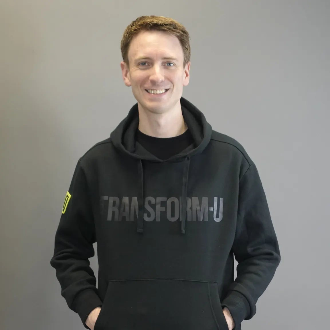 Man wearing a black hoodie with 'TRANSFORM-U' text on a gray background