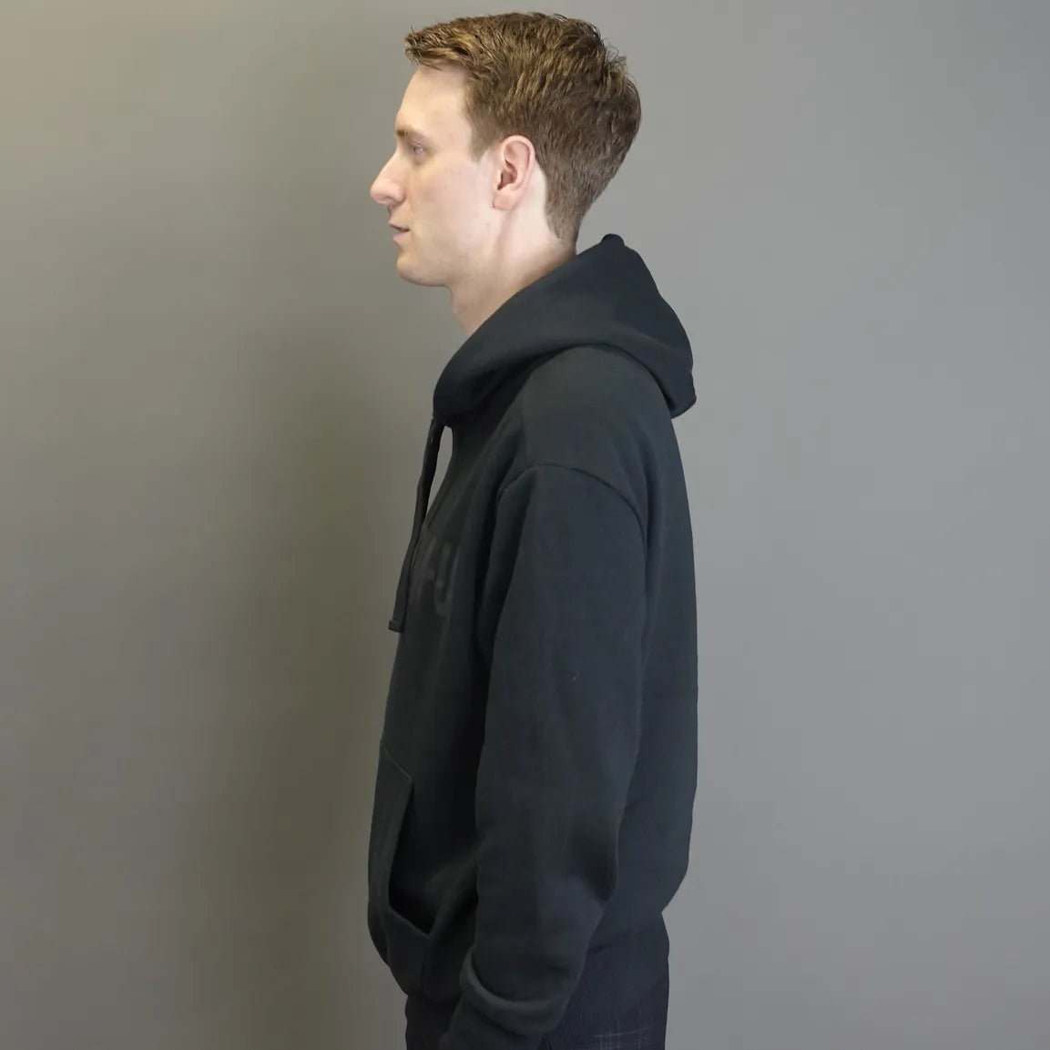 Man wearing a black hoodie standing against a plain gray background