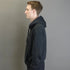 Man wearing a black hoodie standing against a plain gray background