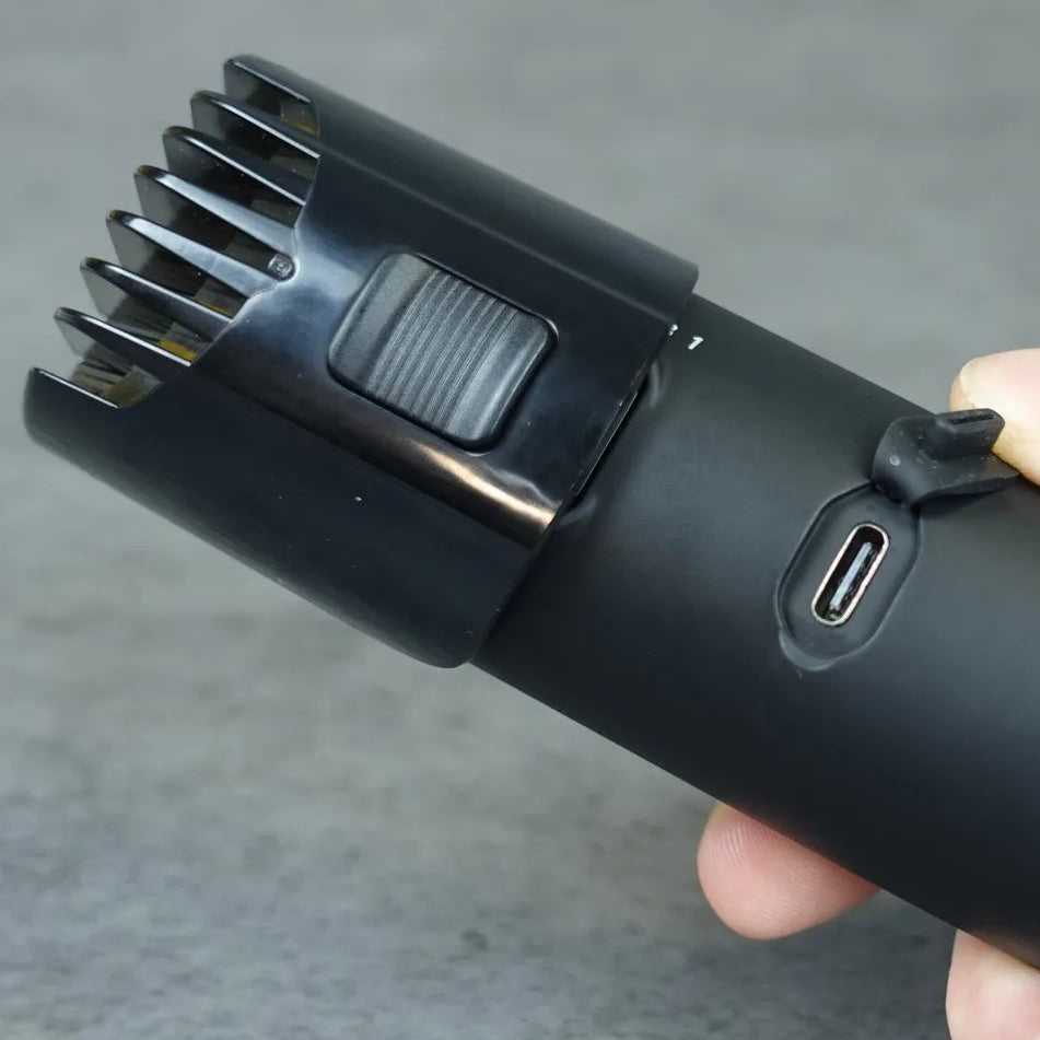 Black body groomer held in a hand with adjustable guide comb against a gray background