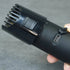 Black body groomer held in a hand with adjustable guide comb against a gray background