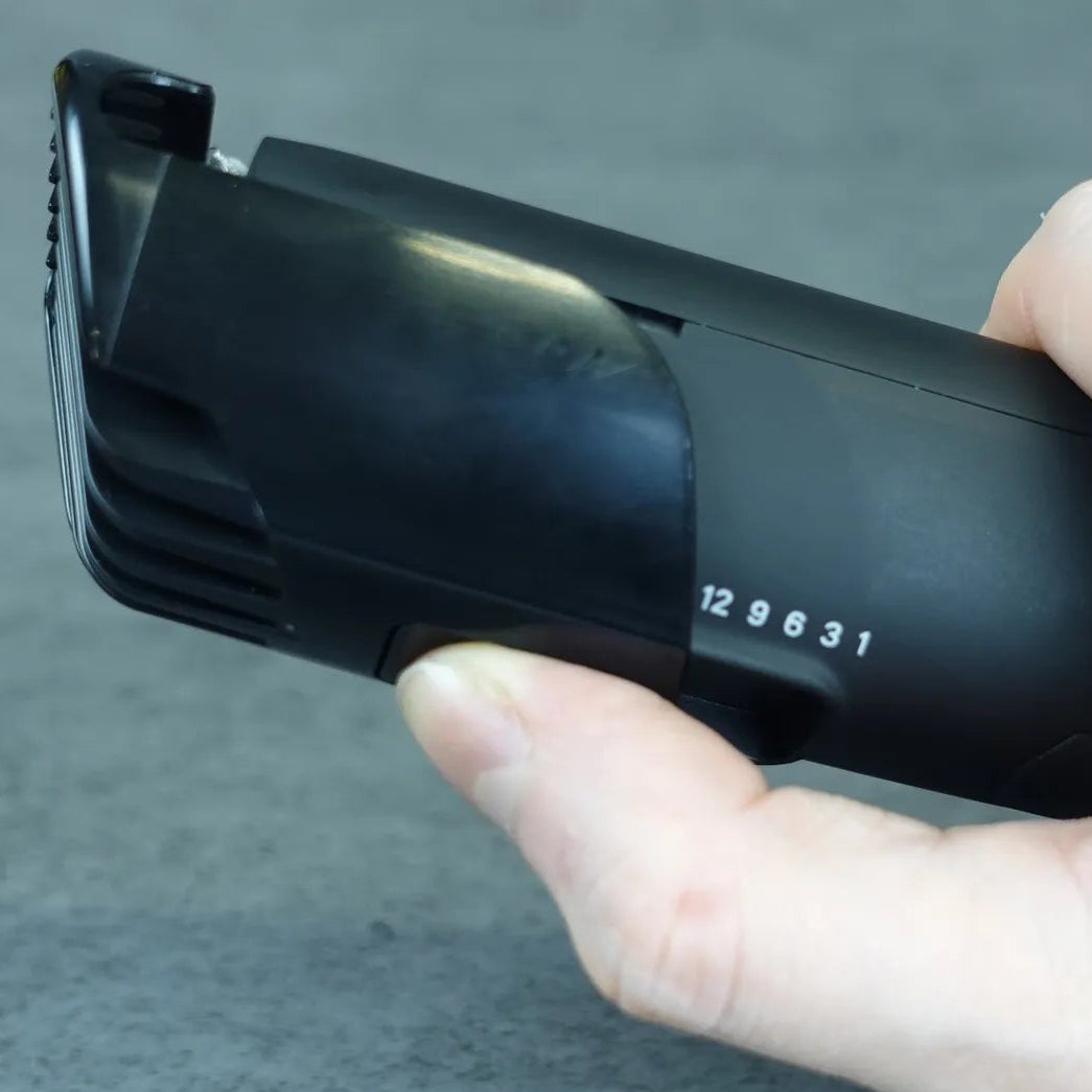 Hand holding a black body groomer with adjustable lengths on a gray background