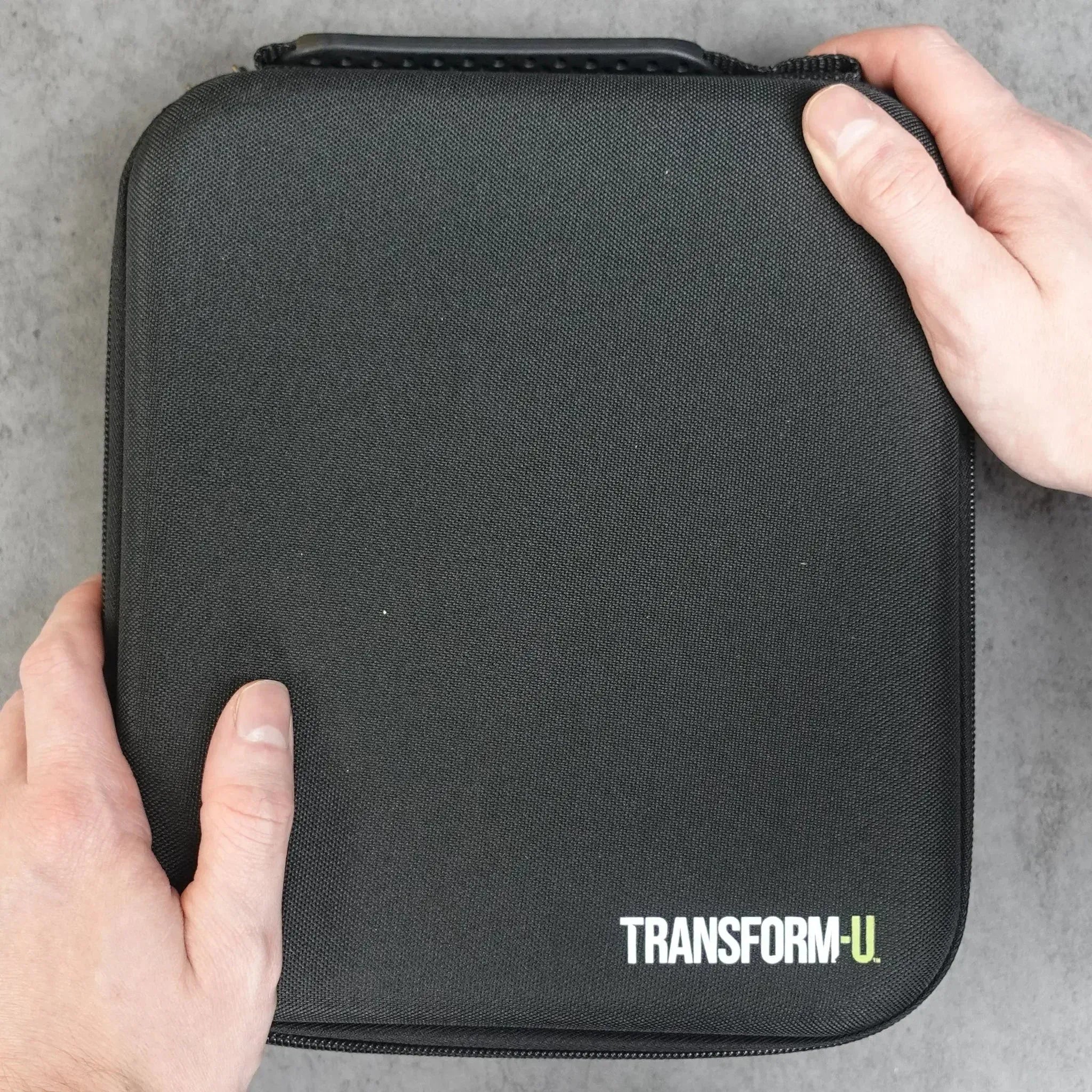 Black carrying case with 'TRANSFORM-U' branding held by hands on a gray background