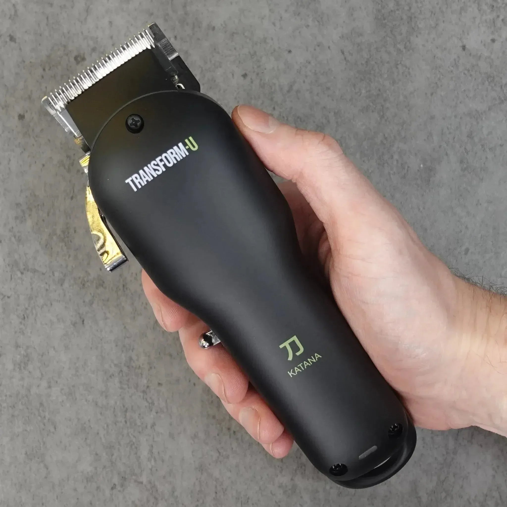Hand holding a black hair clipper with 'TRANSFORM-U' branding on a gray background
