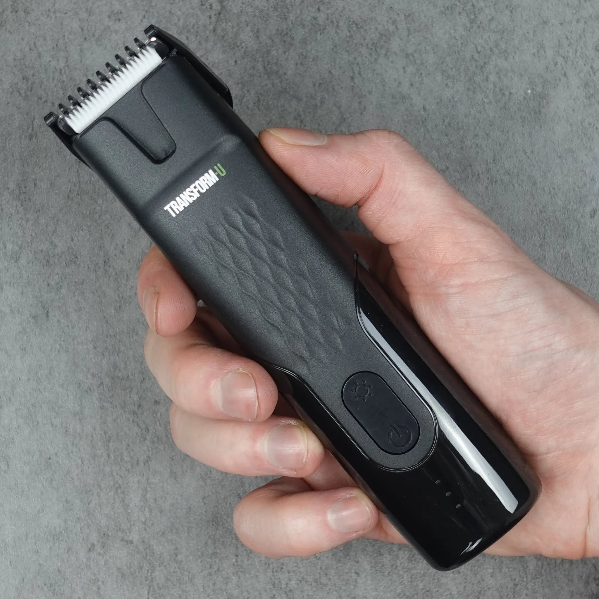 Hand holding a black body grooming tool against a gray background