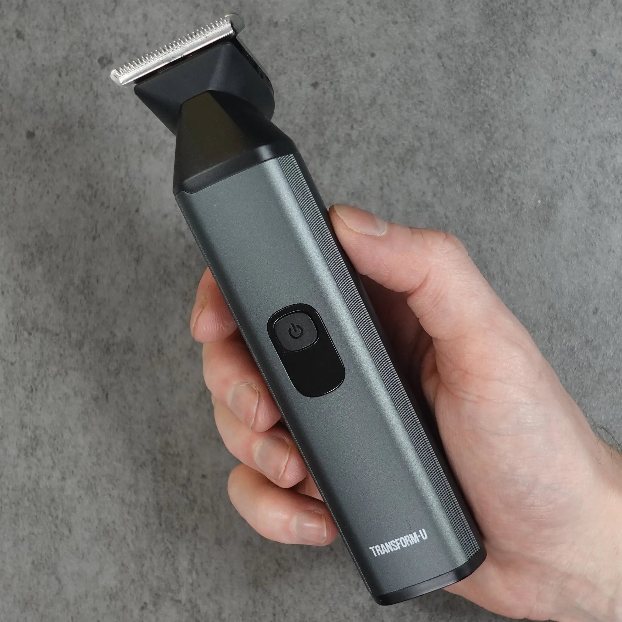 Hand holding a gray beard trimming tool against a concrete wall