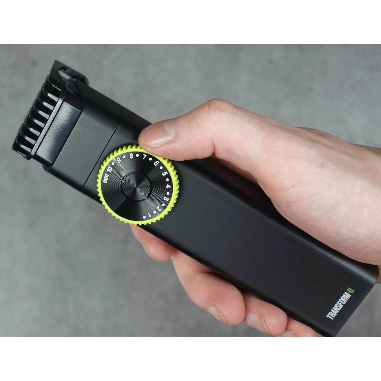 Hand holding a black hair trimmer with a yellow guide comb dial on a gray background