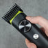 Hand holding a black and green hair trimmer against a gray background