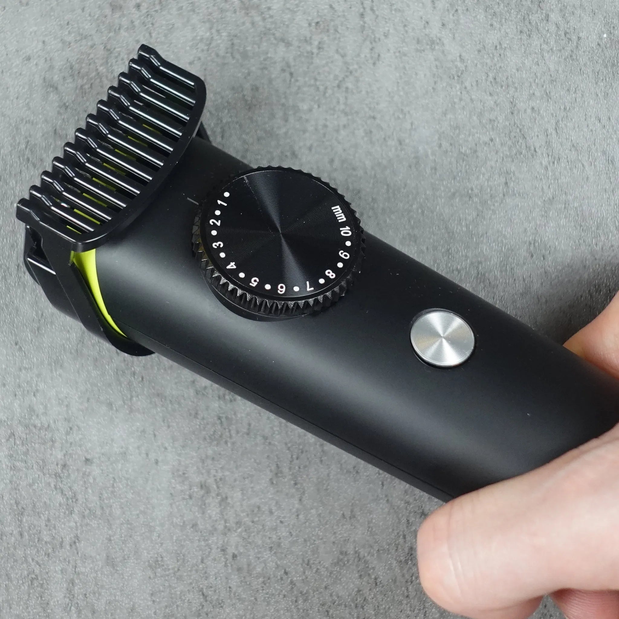 Hand holding a black hair trimmer on a gray surface