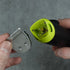 Hand holding a green and black hair trimming tool with a silver blade against a gray background