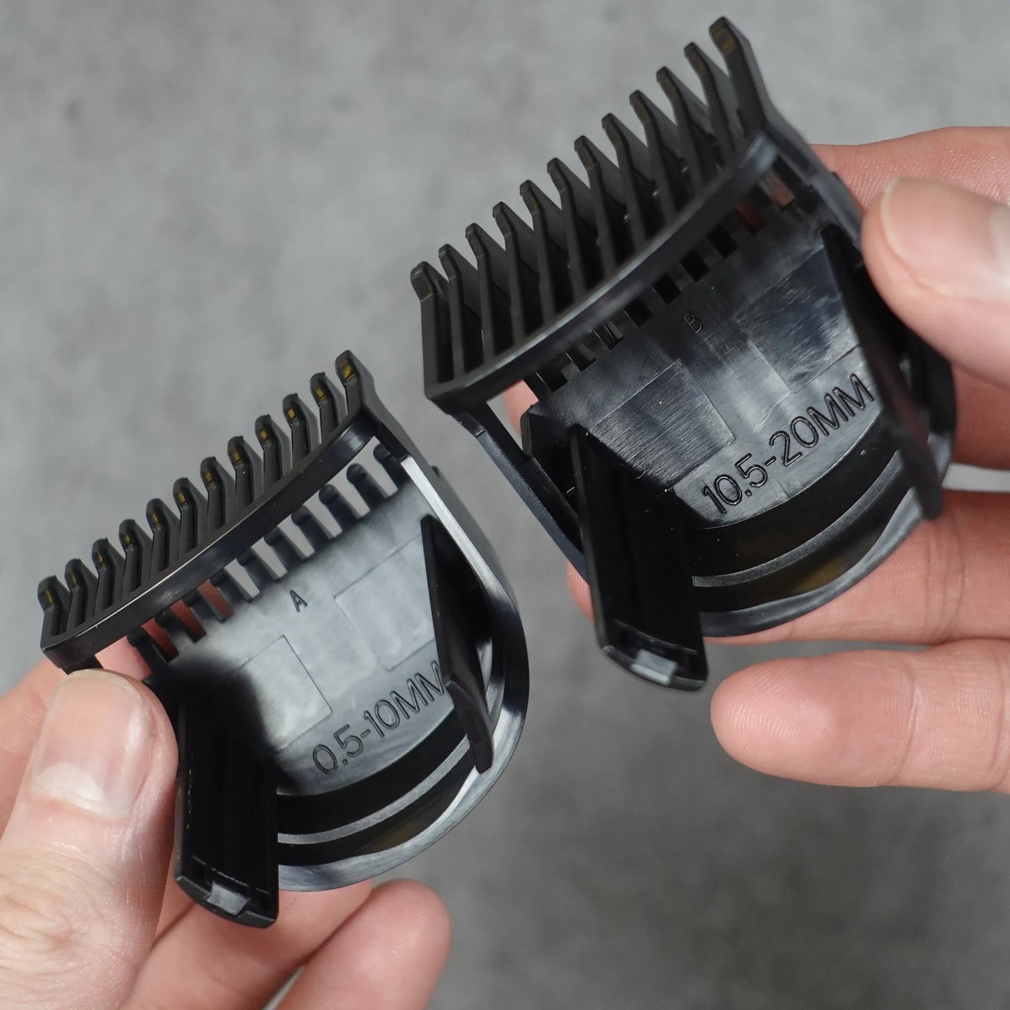 Two black hair trimmer guide combs held by hands against a gray background