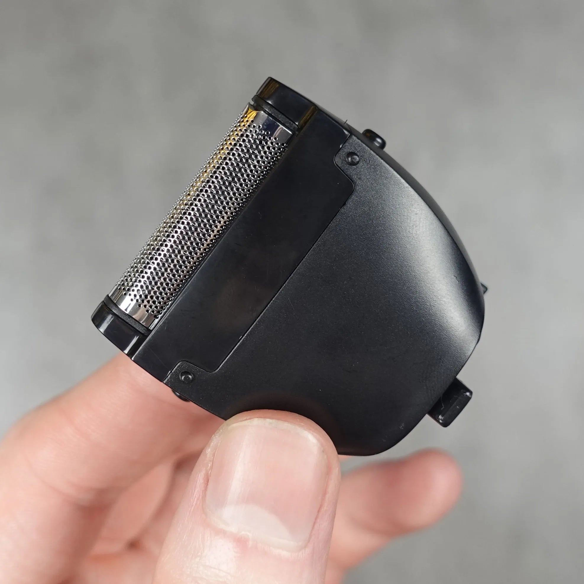 Hand holding a black electric shaver head against a neutral background