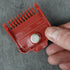 Red hair clipper magnetic guide comb held by a hand on a gray background