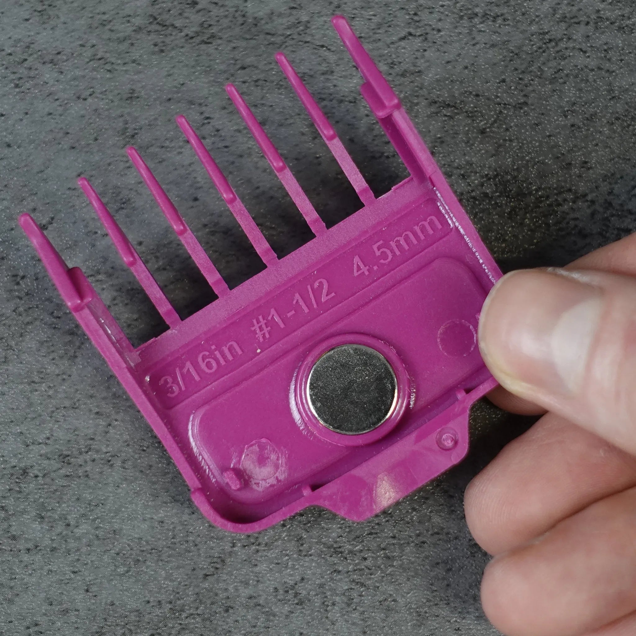 Pink hair clipper magnetic guide comb held by a hand on a gray background