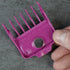 Pink hair clipper magnetic guide comb held by a hand on a gray background