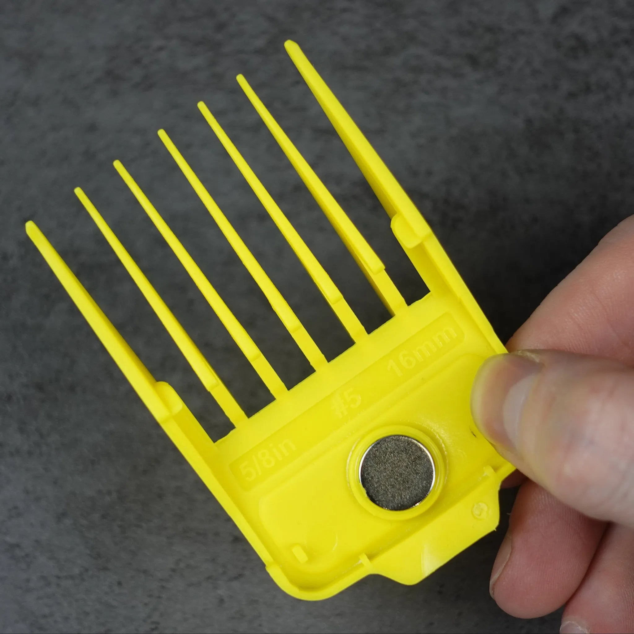 Yellow magnetic guide comb held by a hand against a dark background